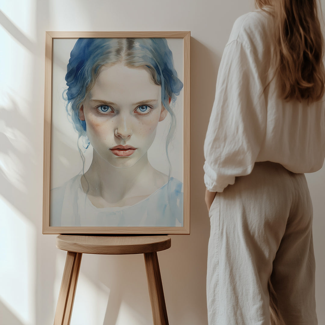 An elegant framed version of 'Wintersoul Decora' resting on a wooden stool, with a woman admiring the artwork in a softly lit space. The portrait’s delicate expression and ethereal hues make it a centerpiece of luxury interiors.